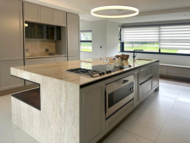 Custom stone kitchen island, counter top and wall cladding by Trend Stone. Stove top on island with modern kettle. Kitchen sink with black tap.